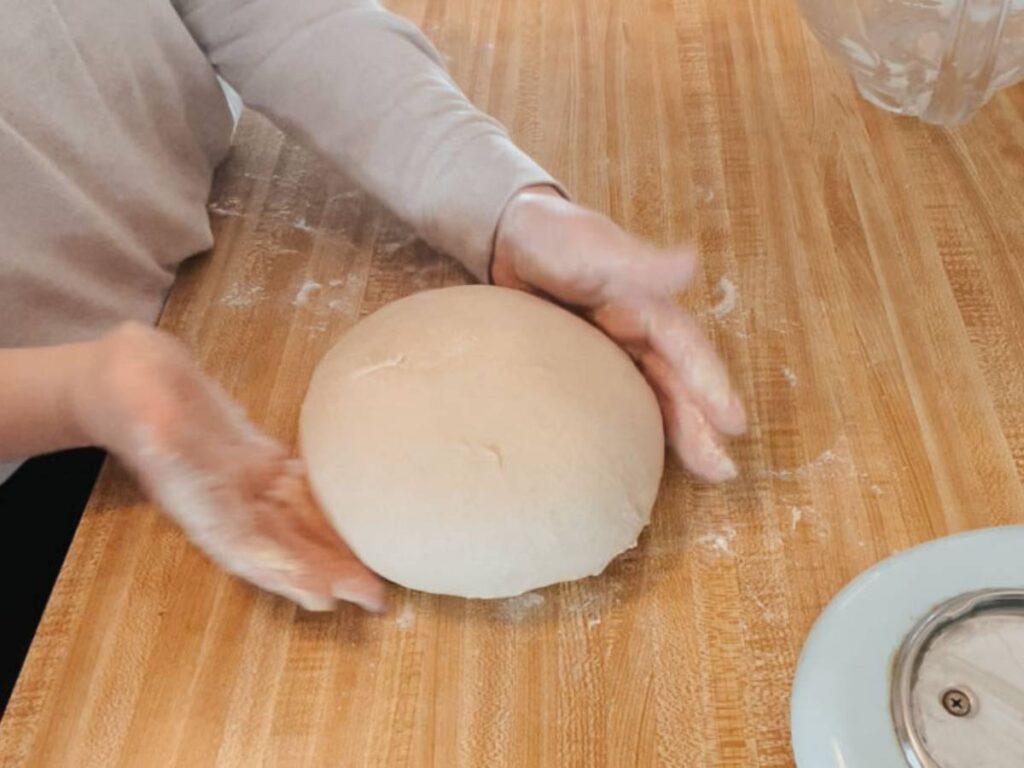 a pair of hands working a ball of sourdough english muffin dough