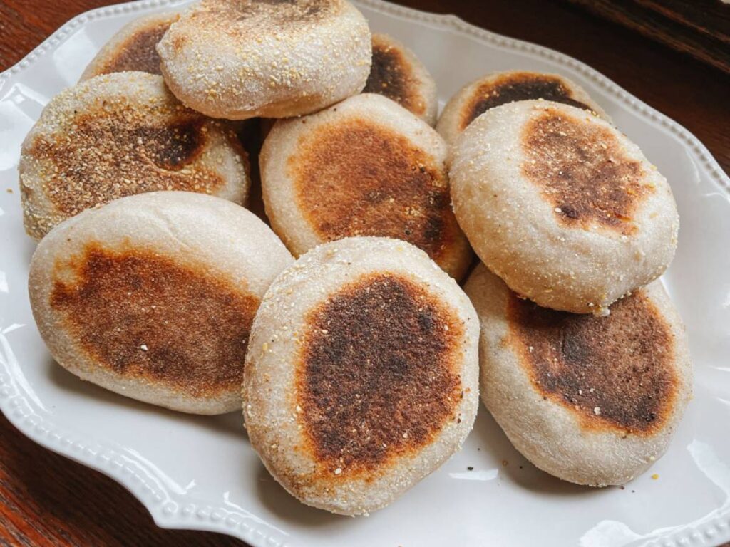 sourdough english muffins piled on a white platter