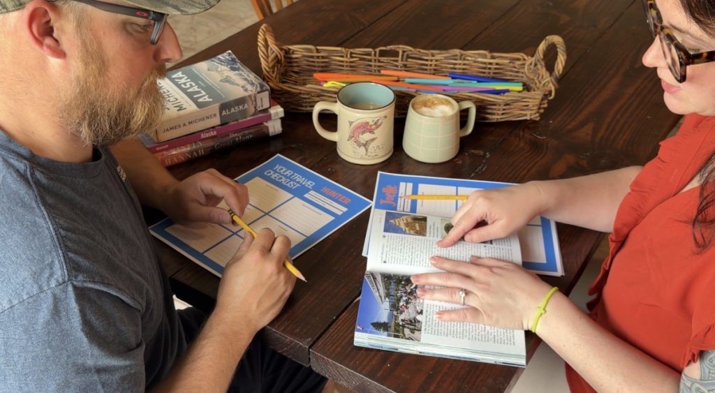 a couple sitting at a table with travel checklists, and books about travel making plans